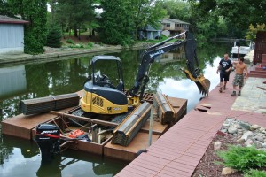 Excavator on a barge on Grand River to install Black Steel Seawall